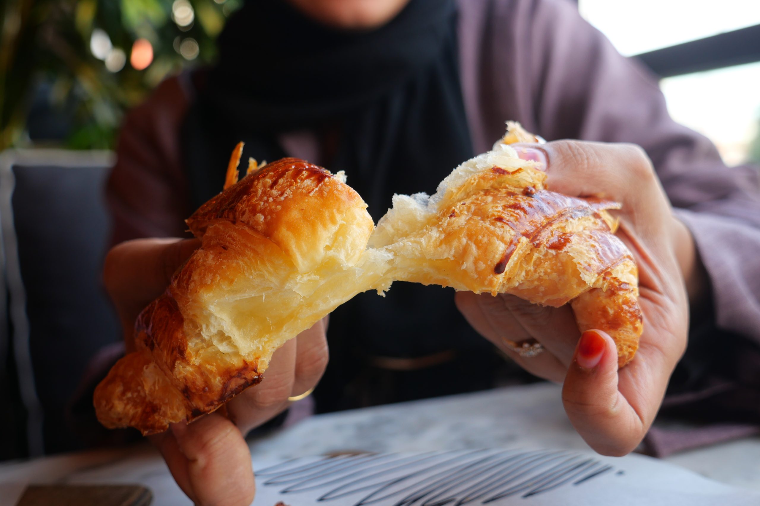 Best Halal Comfort Foods for Winter: Warm, Hearty & Satisfying 13 closeup of hand breaking a croissant bun 2024 12 13 14 23 09 utc scaled